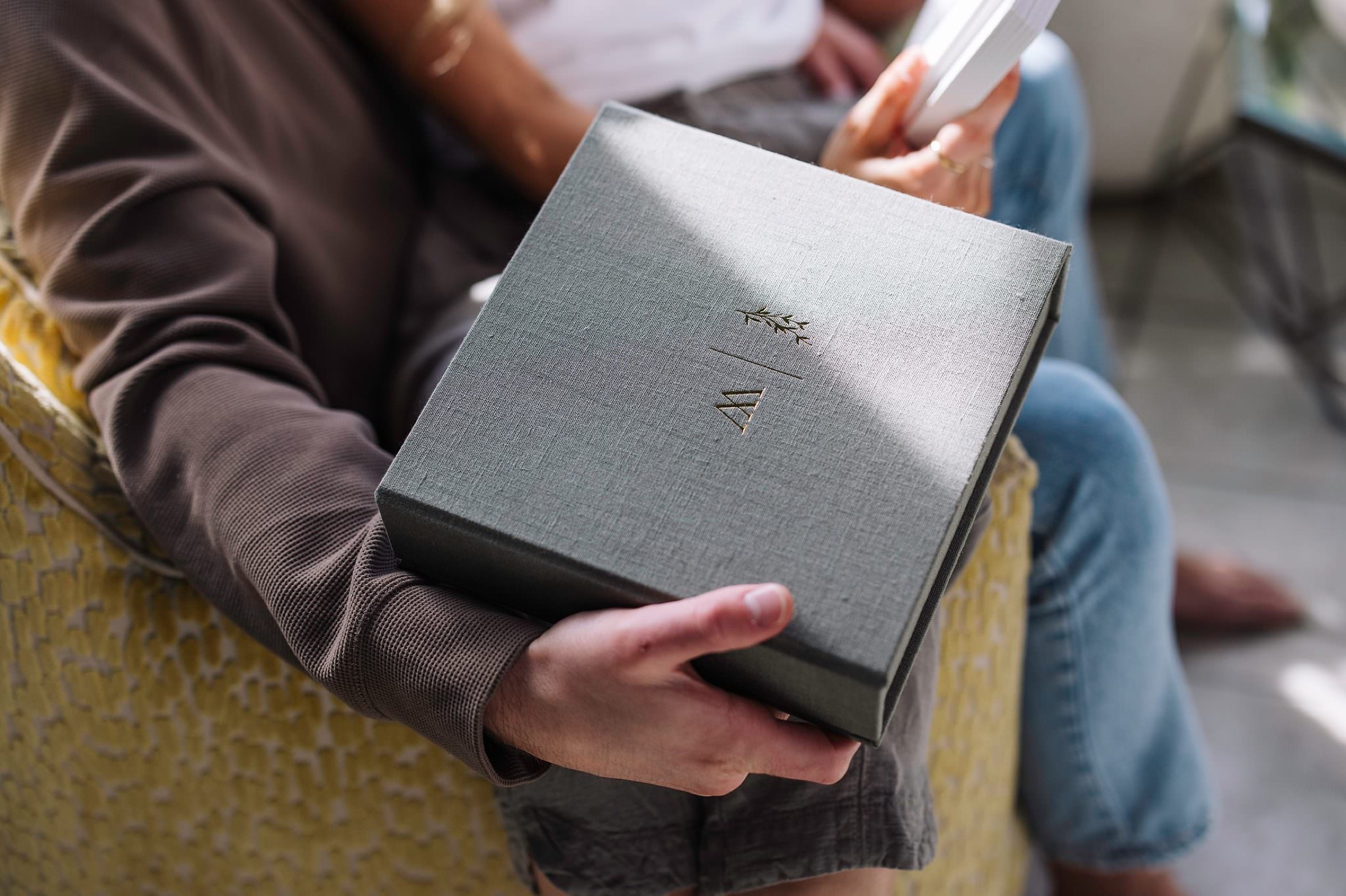 A debossed monogram on the lid of a grey fabric matted print box